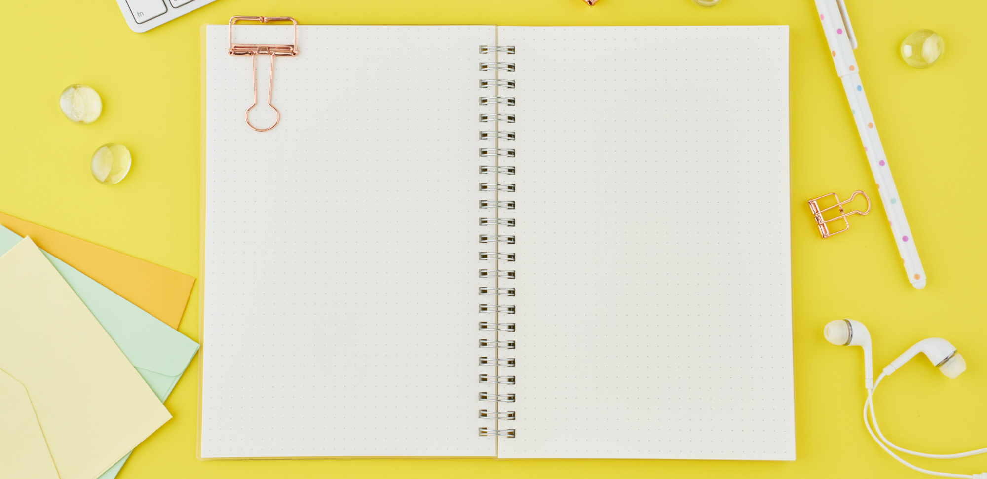 blank journal with dot grid paper laying open on a yellow desk and surrounded by various office supplies